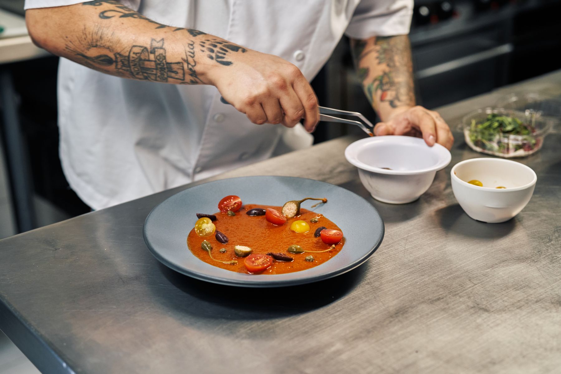 A chef plating a dish with tongs